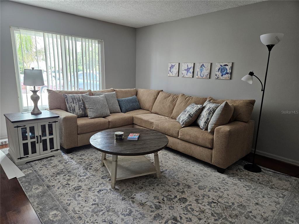 A living room features a tan sectional sofa, a round wooden coffee table, and coastal wall art — 206 SOLA LANE, SUN CITY CENTER, FL