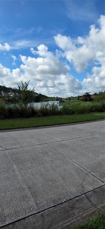 A concrete driveway overlooks a grassy bank and a small lake under a cloudy sky — BELLERIVE DRIVE, CLERMONT, FL