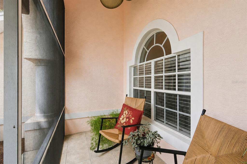 A screened-in porch features light-colored tile flooring, peach-colored walls, and a large arched window — 1518 FISHING LAKE DRIVE, ODESSA, FL