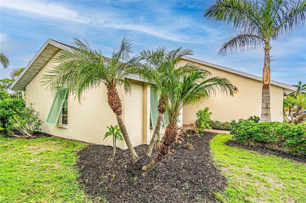 The exterior of a beige house features green shutters, a palm tree, and landscaped mulch beds — 1501 63RD STREET W, BRADENTON, FL