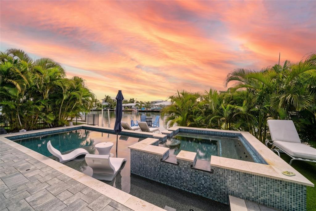 A swimming pool and spa overlook a canal at sunset with lounge chairs and palm trees — 501 68TH STREET, HOLMES BEACH, FL