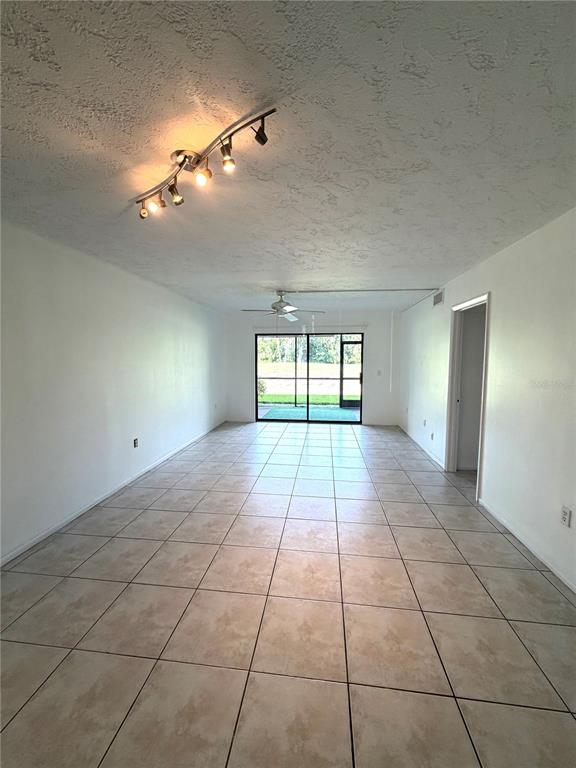 A long, tiled living room features a track light, ceiling fan, and sliding glass doors — 7750 EAGLE CREEK DRIVE UNIT 7750, SARASOTA, FL