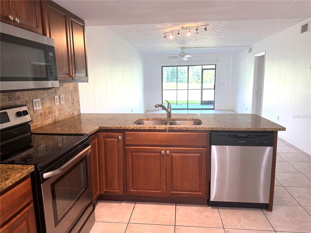 A kitchen with wood cabinets, granite countertops, and stainless steel appliances overlooks a living area — 7750 EAGLE CREEK DRIVE UNIT 7750, SARASOTA, FL
