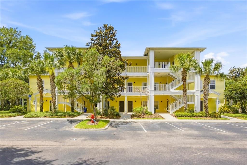 A three-story yellow apartment building features exterior staircases, white railings, and palm trees — 808 LUCAYA LOOP, DAVENPORT, FL