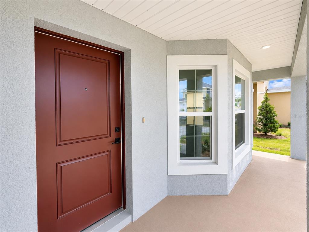 A red front door opens onto a covered porch with light gray stucco walls — 7642 BENT TREE LOOP, ST CLOUD, FL