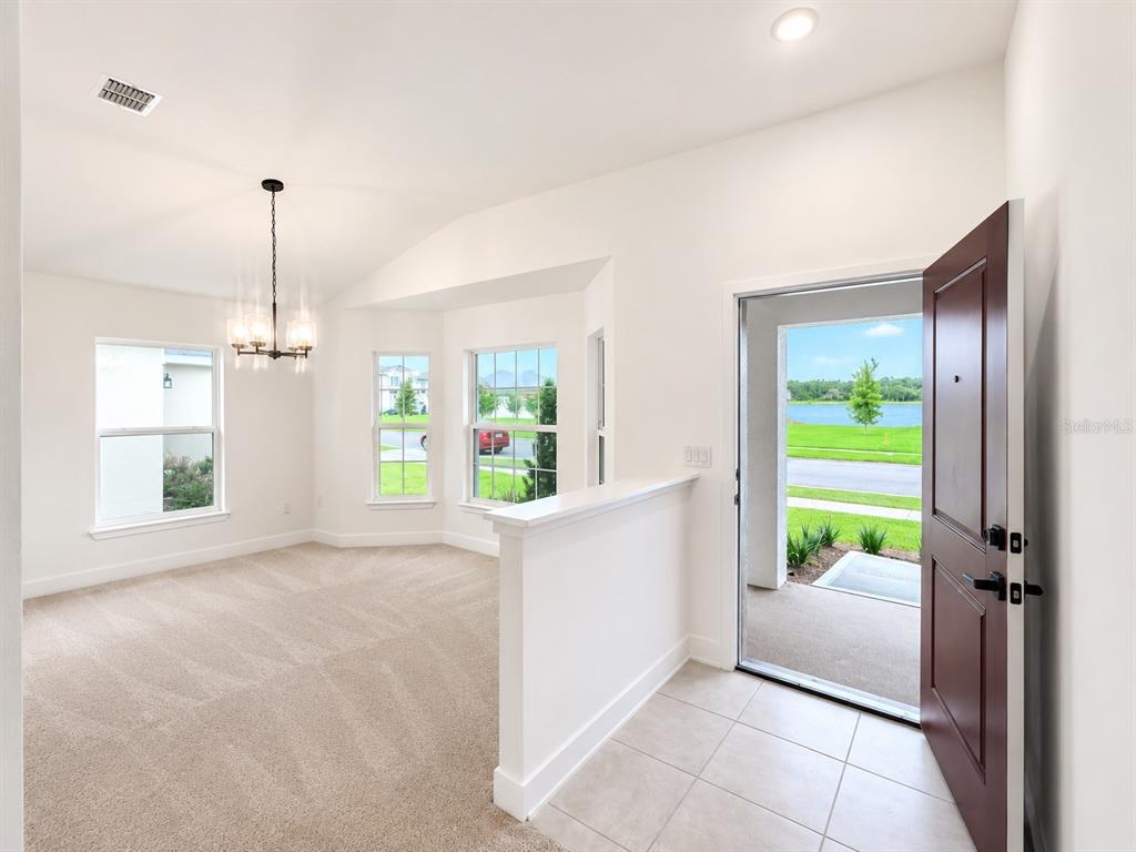 A carpeted dining area with a chandelier sits next to a tiled entryway and front door — 7642 BENT TREE LOOP, ST CLOUD, FL