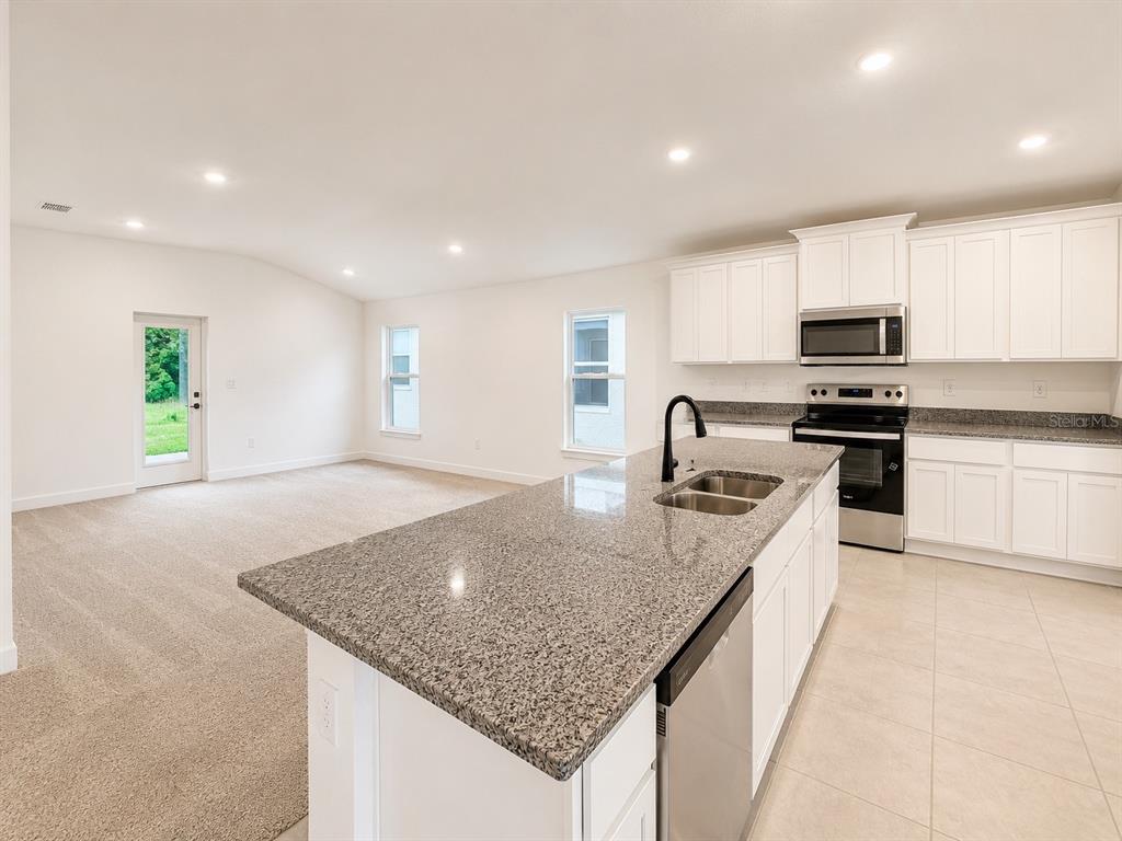 A kitchen with granite countertops and white cabinets overlooks an open-concept carpeted living area — 7642 BENT TREE LOOP, ST CLOUD, FL