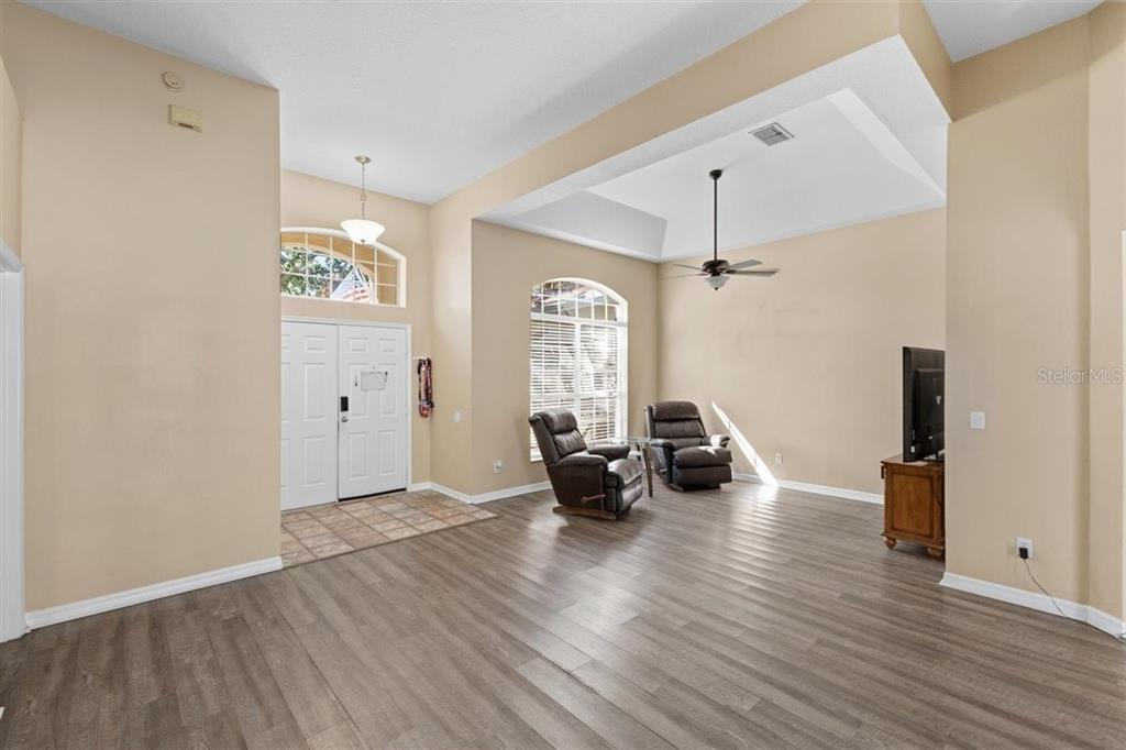 A living room with high ceilings, wood-look flooring, two leather recliners, and a double-door entrance — 7909 FERNLEAF DRIVE, ORLANDO, FL