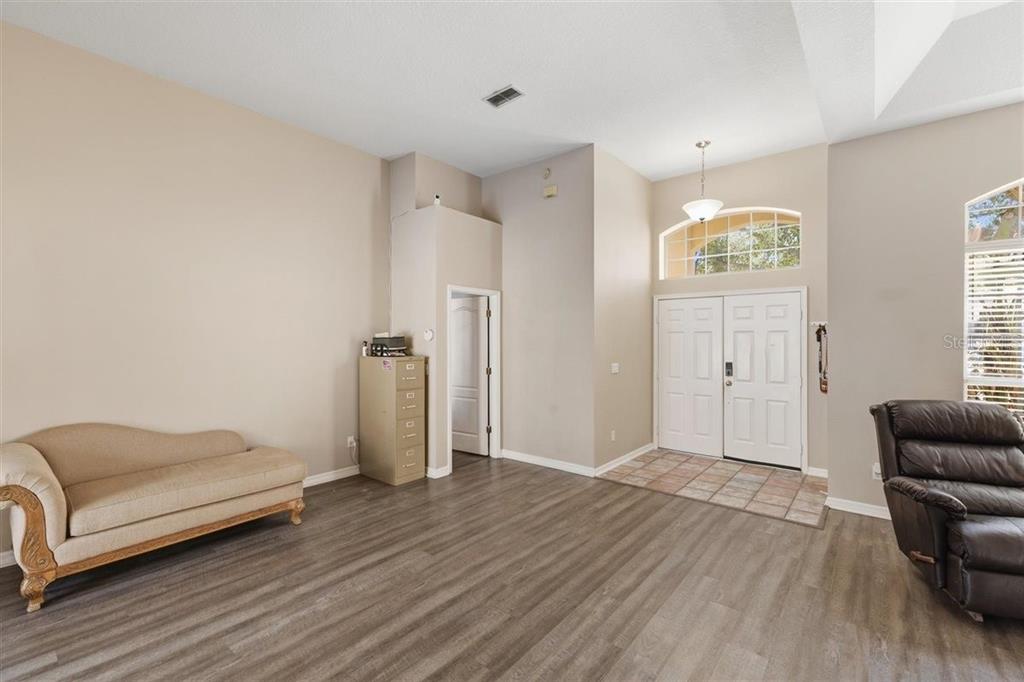 A high-ceilinged entryway features wood-look flooring, a beige fainting couch, and double front doors — 7909 FERNLEAF DRIVE, ORLANDO, FL