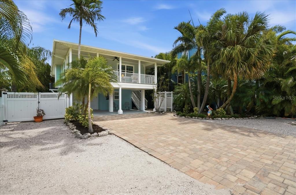 A stilt house with a paved driveway, white fence, and palm trees under a blue sky — 2811 GULF DRIVE, HOLMES BEACH, FL