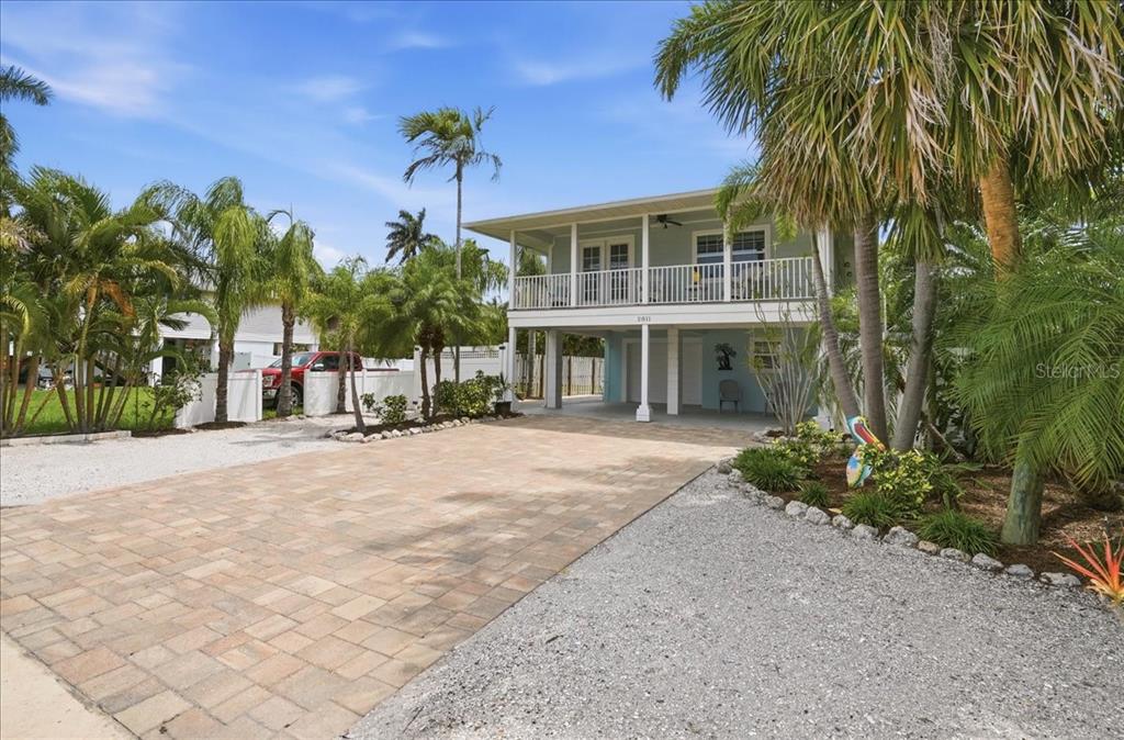 A two-story house with a raised balcony, paved driveway, and palm trees in the yard — 2811 GULF DRIVE, HOLMES BEACH, FL