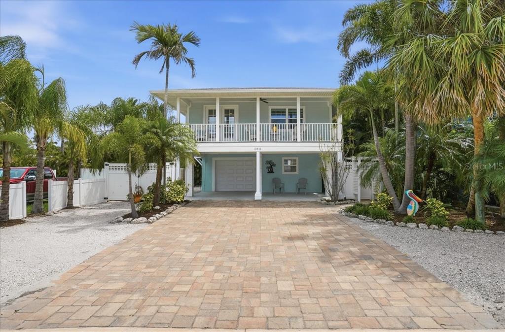 A two-story house with a paved driveway, a garage, and a balcony sits among palm trees — 2811 GULF DRIVE, HOLMES BEACH, FL