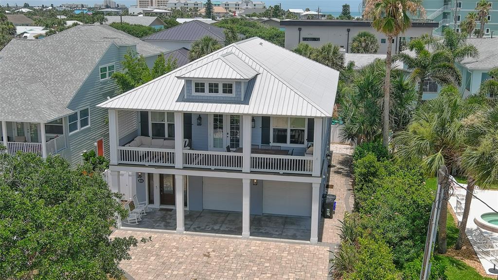 An elevated two-story house with a metal roof, a large balcony, and a paved driveway — 818 OCEAN AVENUE, NEW SMYRNA BEACH, FL