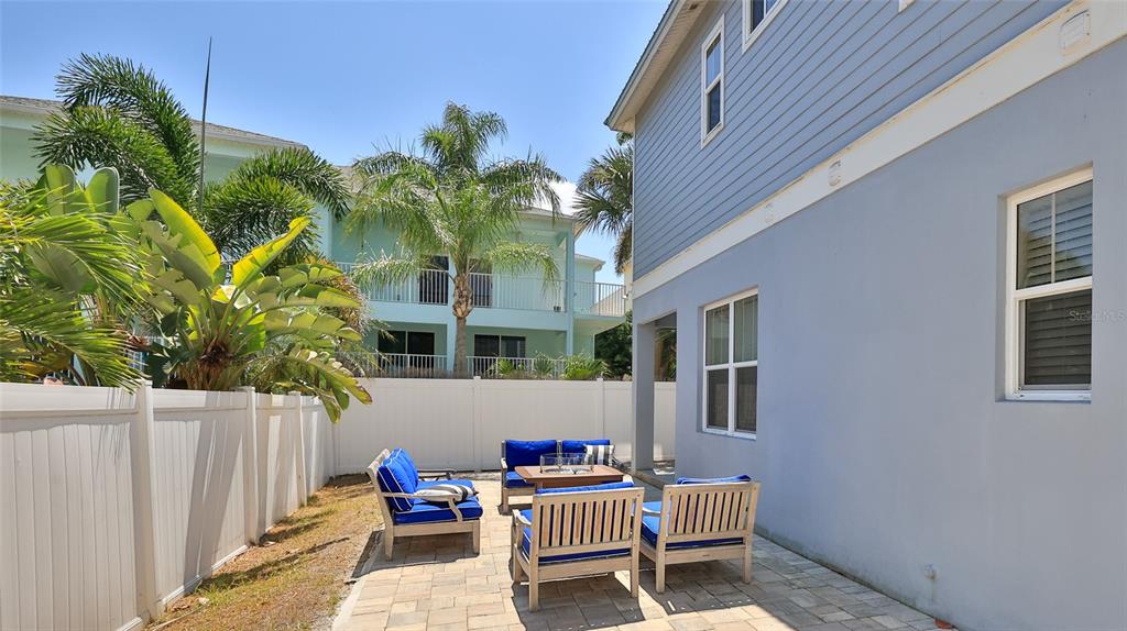 A paved patio with outdoor furniture sits beside a blue house with a white fence — 818 OCEAN AVENUE, NEW SMYRNA BEACH, FL