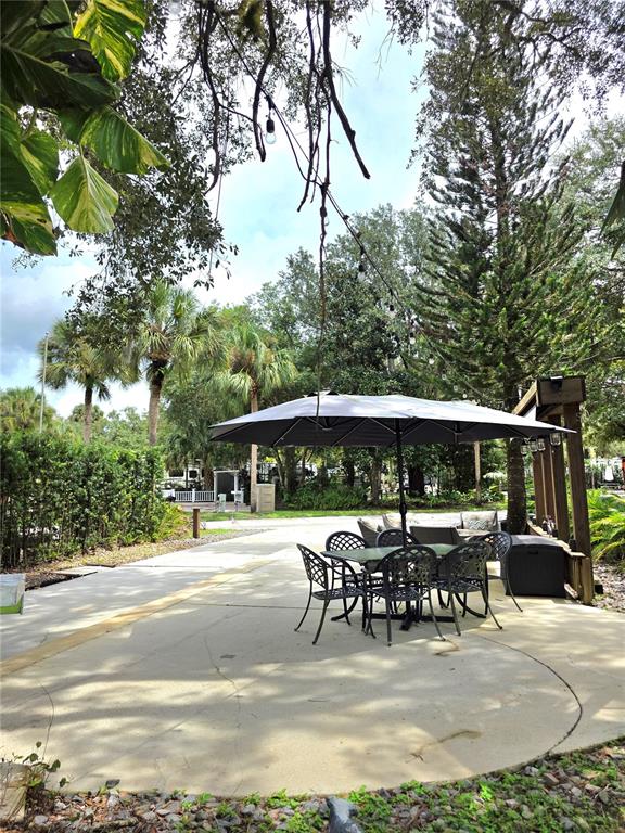 A patio features a dining set with an umbrella, a swing, and a grill outdoors — 159 HORSESHOE BEND, LAKE WALES, FL
