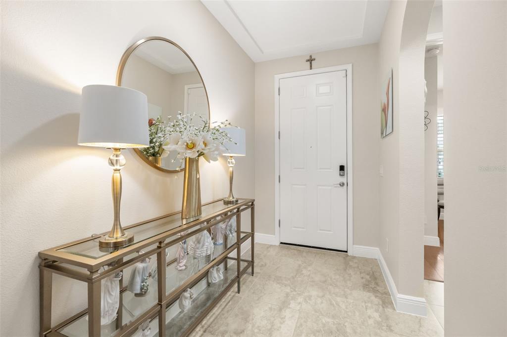 A bright entryway features a glass-topped console table, two lamps, a round mirror, and tile flooring — 17307 BAL HARBOUR DRIVE, WINTER GARDEN, FL