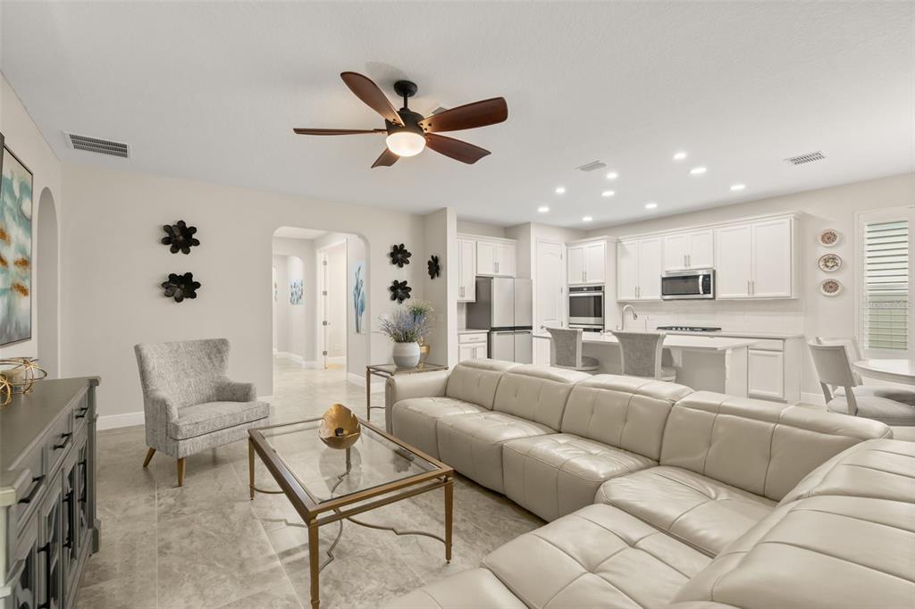 An open-concept living room features a large sectional sofa, a glass coffee table, and kitchen — 17307 BAL HARBOUR DRIVE, WINTER GARDEN, FL