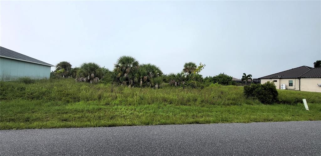 A vacant, grassy residential lot with scattered palm trees situated between two existing houses — 9316 GALAXIE CIRCLE, PORT CHARLOTTE, FL