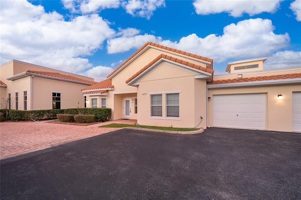 A one-story stucco house with a tile roof, a garage, and a paved driveway — 1075 DAVID WALKER DRIVE UNIT C-1, TAVARES, FL