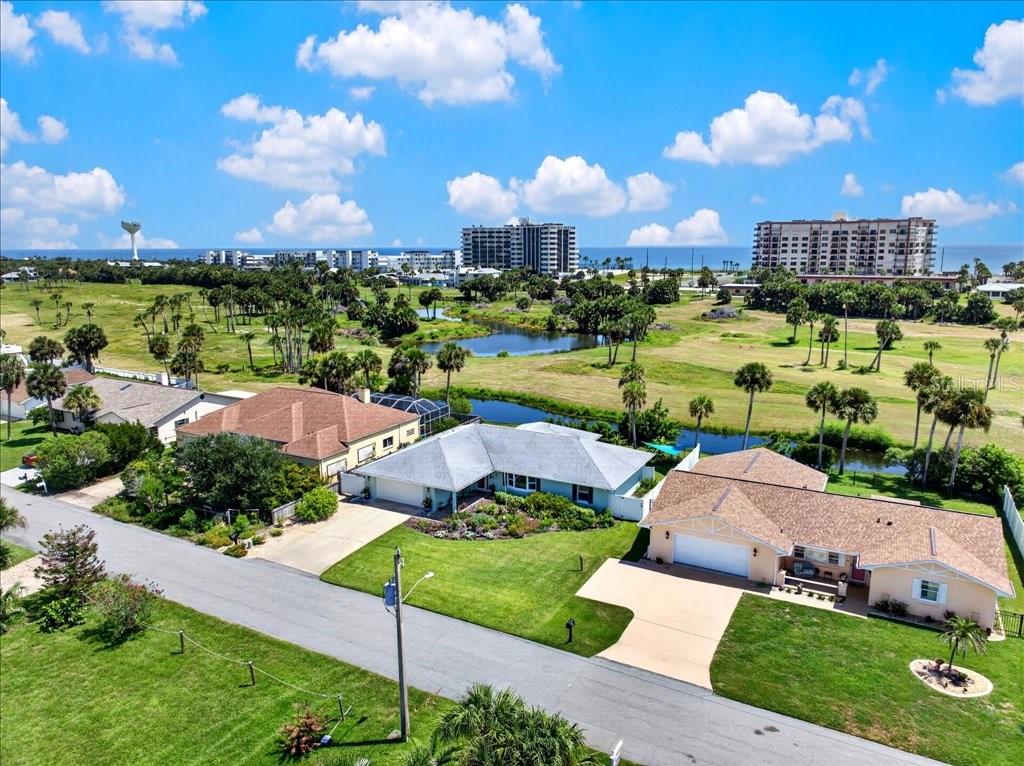 An aerial view of three suburban houses near a pond with oceanfront buildings in the distance — 263 OCEAN PALM DRIVE, FLAGLER BEACH, FL