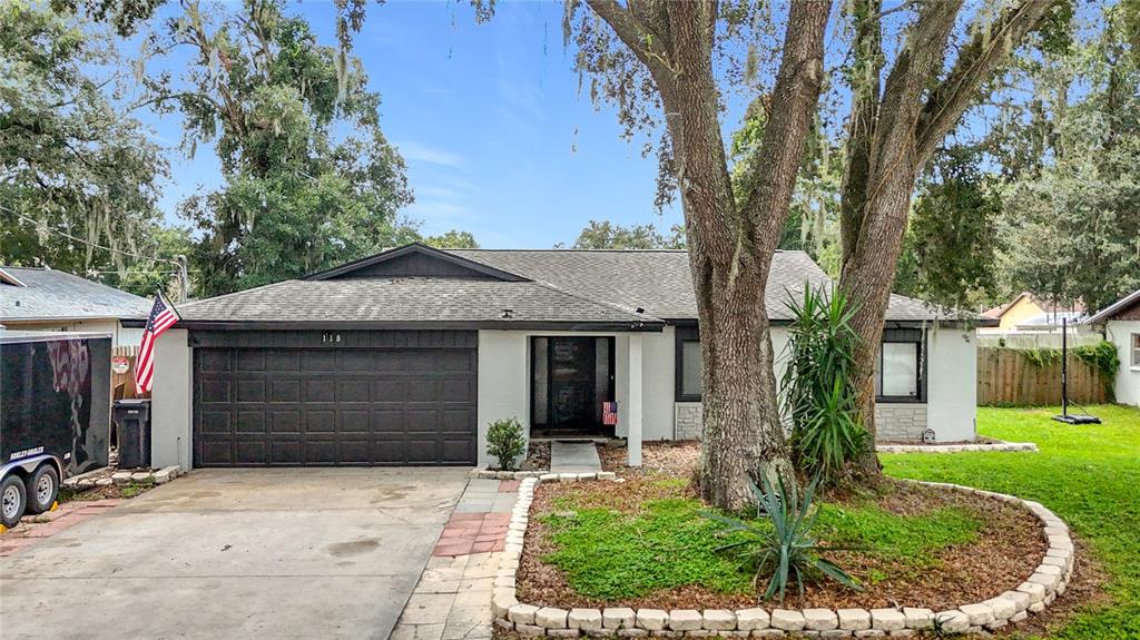 A single-story house with a dark garage door, a front yard tree, and a stone planter — 118 EUCLID LOOP, SEFFNER, FL