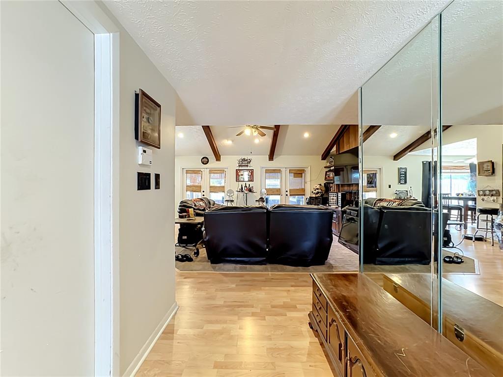A hallway with wood flooring leads into a living room featuring vaulted ceilings and mirrors — 118 EUCLID LOOP, SEFFNER, FL