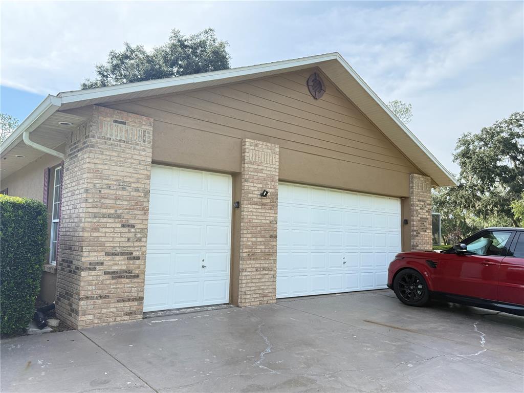 A house exterior features a two-car garage with white doors and tan brick accents — 7613 NW 46TH STREET, OCALA, FL