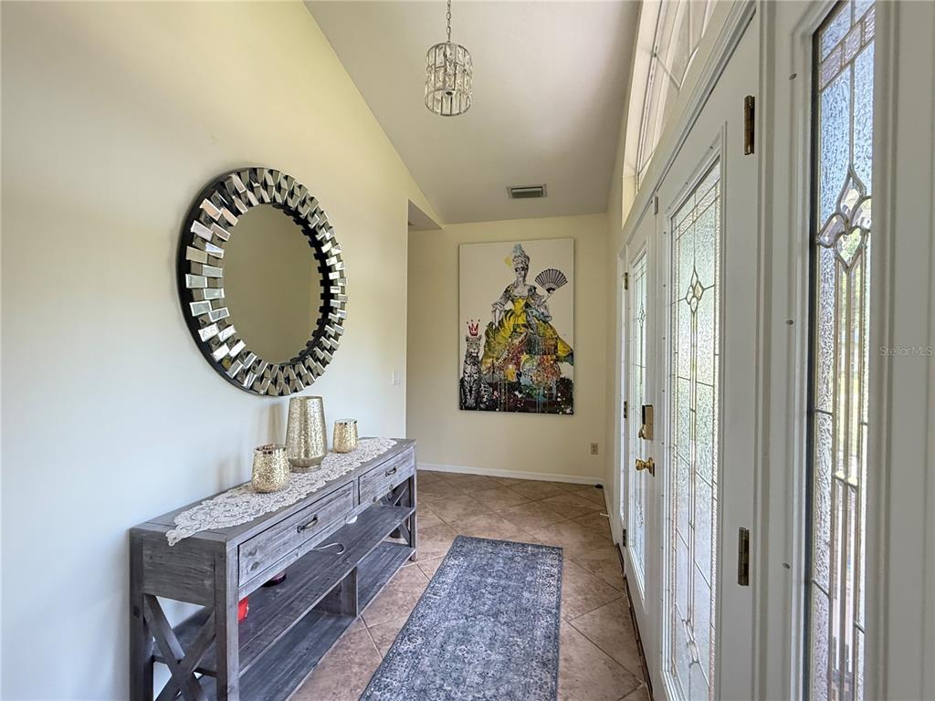 A foyer features a console table, a round mirror, a large painting, and tile flooring — 7613 NW 46TH STREET, OCALA, FL
