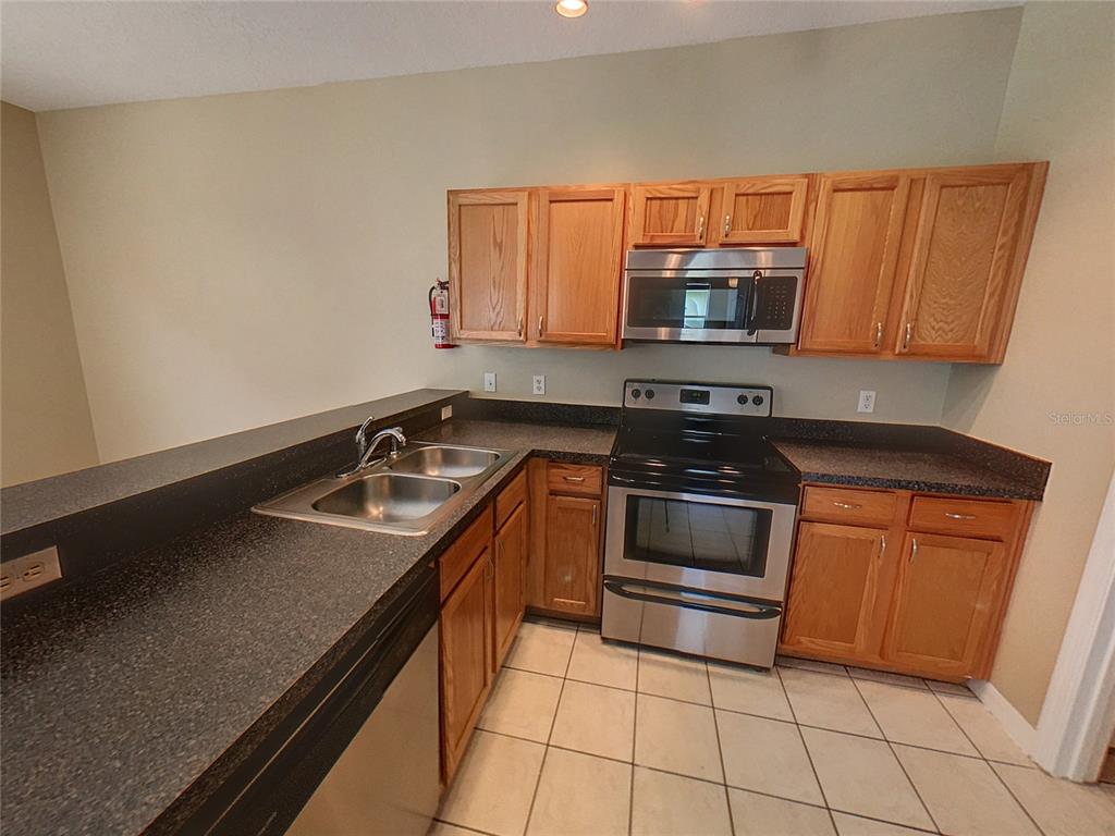 A kitchen features wooden cabinets, stainless steel appliances, and dark countertops over tiled flooring — 124 HAMMOCK COURT, DAVENPORT, FL