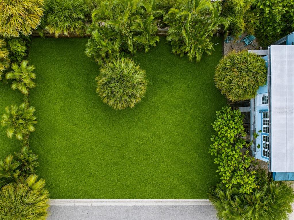 An aerial view shows a lush green lawn surrounded by palm trees and a house — 131 86TH TERRACE, TREASURE ISLAND, FL