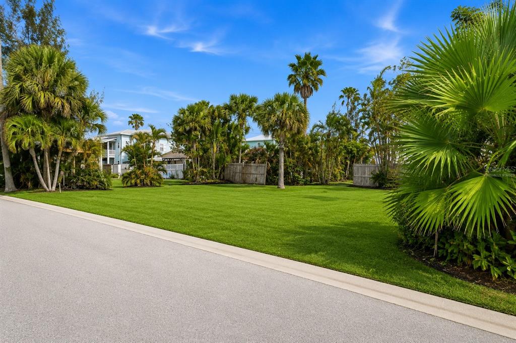A grassy vacant lot is surrounded by palm trees and a wooden fence — 131 86TH TERRACE, TREASURE ISLAND, FL