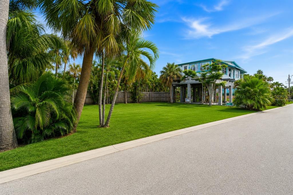 A stilt house sits behind a large green lawn surrounded by palm trees and foliage — 131 86TH TERRACE, TREASURE ISLAND, FL
