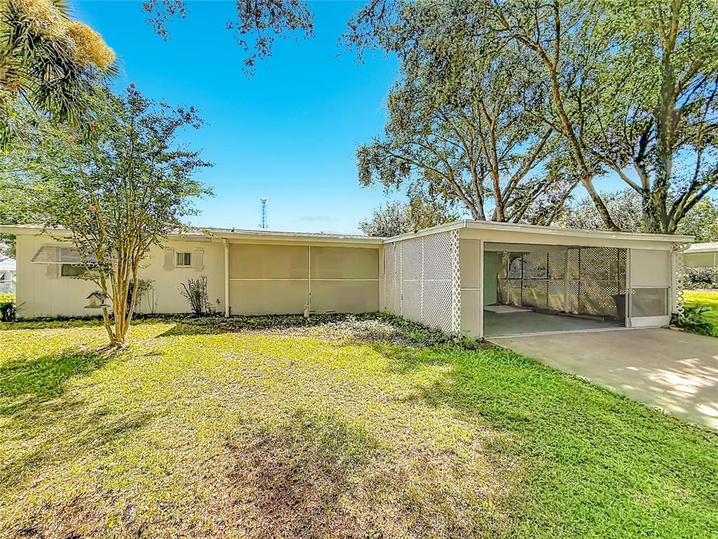 The exterior of a single-story home features a screened-in carport and a grassy yard — 10035 SW 91ST TERRACE, OCALA, FL