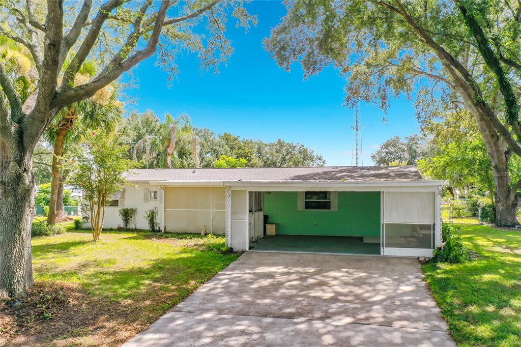 A single-story house with a green-painted carport and a concrete driveway under large trees — 10035 SW 91ST TERRACE, OCALA, FL