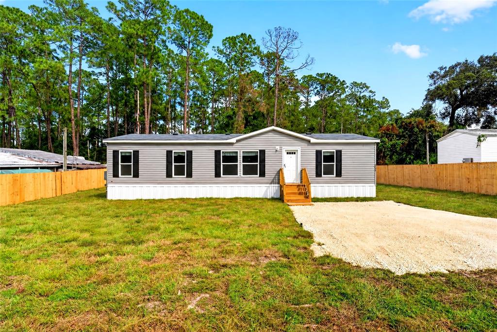 A single-story manufactured home with grey siding, black shutters, and a wooden front porch — 5759 SE 184 TERRACE, OCKLAWAHA, FL
