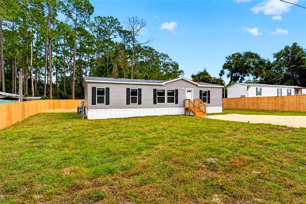 A single-story manufactured home with gray siding sits on a dirt lot with wooden stairs — 5759 SE 184 TERRACE, OCKLAWAHA, FL