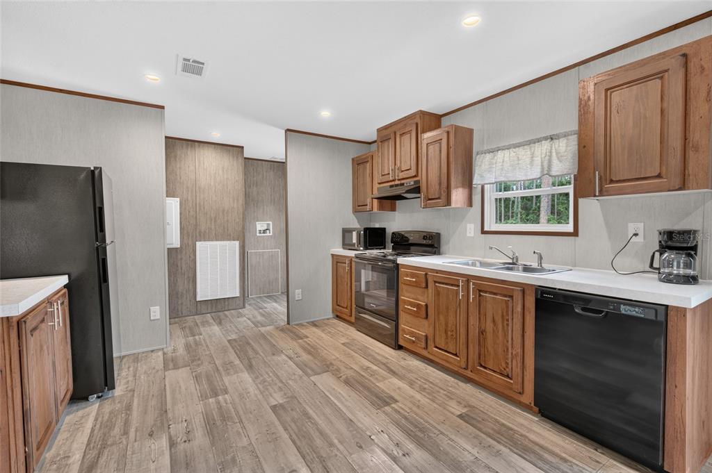 A kitchen features dark wood cabinets, black appliances, white countertops, and light wood-look flooring — 5759 SE 184 TERRACE, OCKLAWAHA, FL