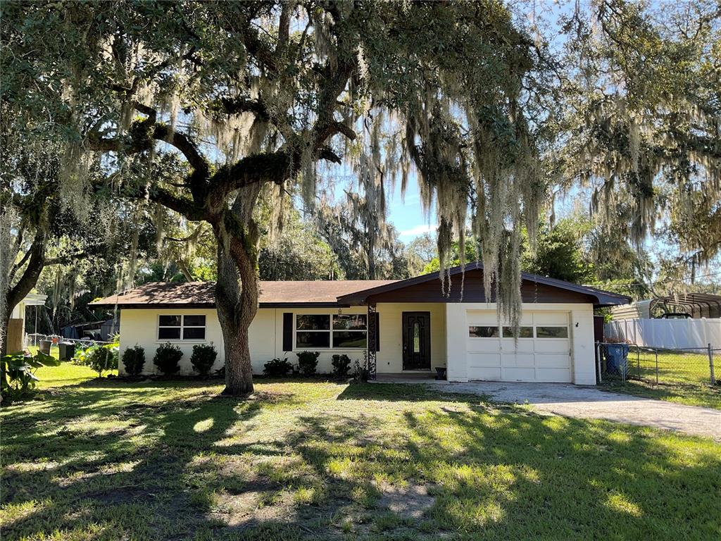 A single-story house with a white exterior, a brown roof, and a large oak tree — 5032 FLAMINGO LANE, DADE CITY, FL