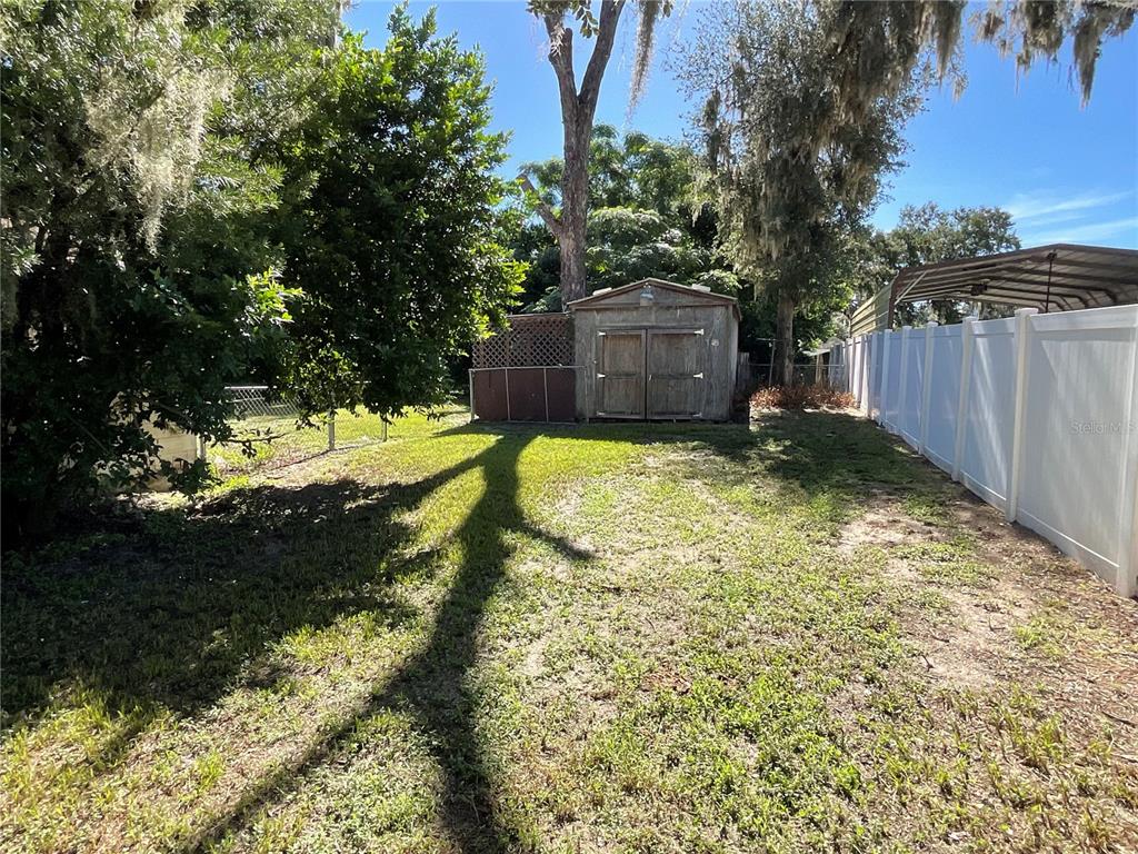 A backyard features a wooden shed, a white vinyl fence, and mature trees — 5032 FLAMINGO LANE, DADE CITY, FL