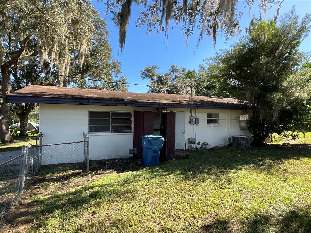 The exterior of a single-story white house features a brown roof and a blue trash bin — 5032 FLAMINGO LANE, DADE CITY, FL