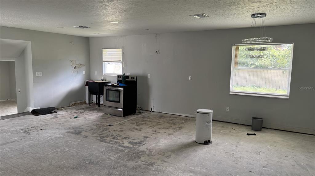 An unfinished kitchen area features gray walls, a stainless steel stove, and bare concrete floors — 2189 SUSSEX ROAD, WINTER PARK, FL
