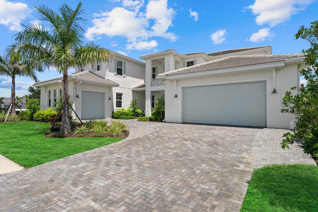 A two-story white house with a paver driveway and two garage doors under a blue sky — 8129 NEVIS RUN, LAKEWOOD RANCH, FL
