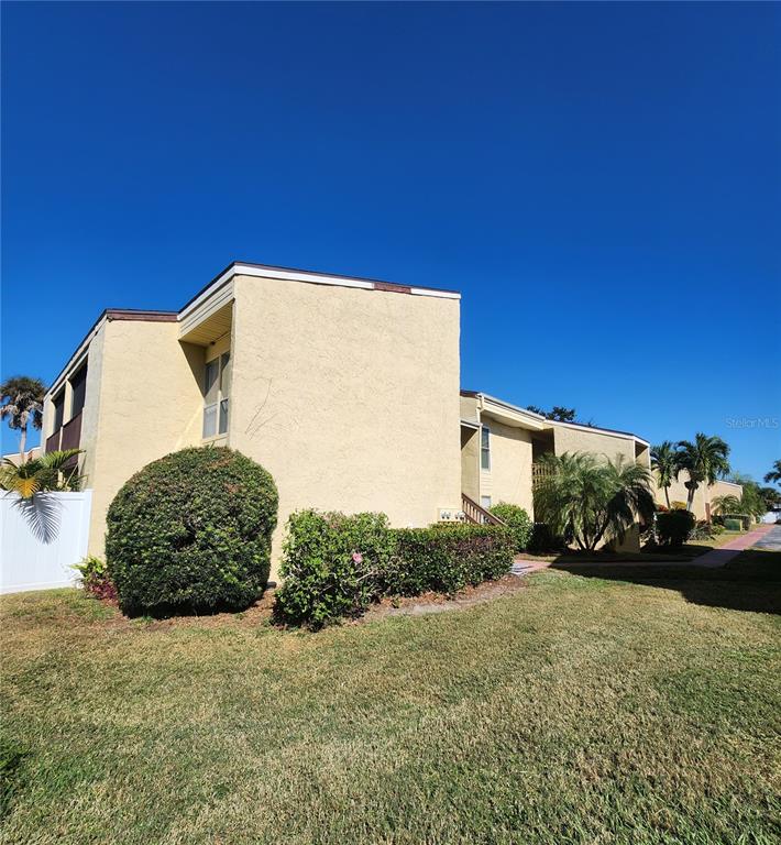 A two-story tan apartment building with a grassy lawn and landscaping under a clear sky — 3415 CLARK ROAD UNIT 215, SARASOTA, FL