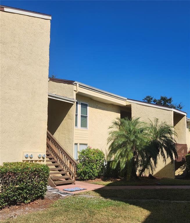 A two-story tan stucco apartment building features an exterior wooden staircase and palm trees — 3415 CLARK ROAD UNIT 215, SARASOTA, FL