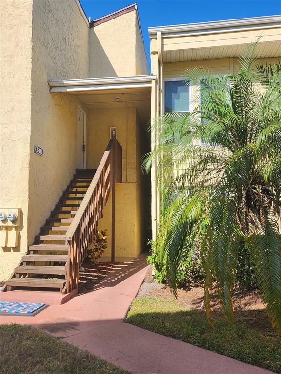 An exterior view of a yellow building with a wooden staircase leading to an upper entrance — 3415 CLARK ROAD UNIT 215, SARASOTA, FL