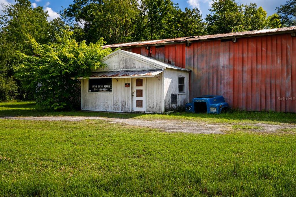 A weathered white office structure is attached to a large red metal industrial building — 103 CONTAINER ROAD, STARKE, FL