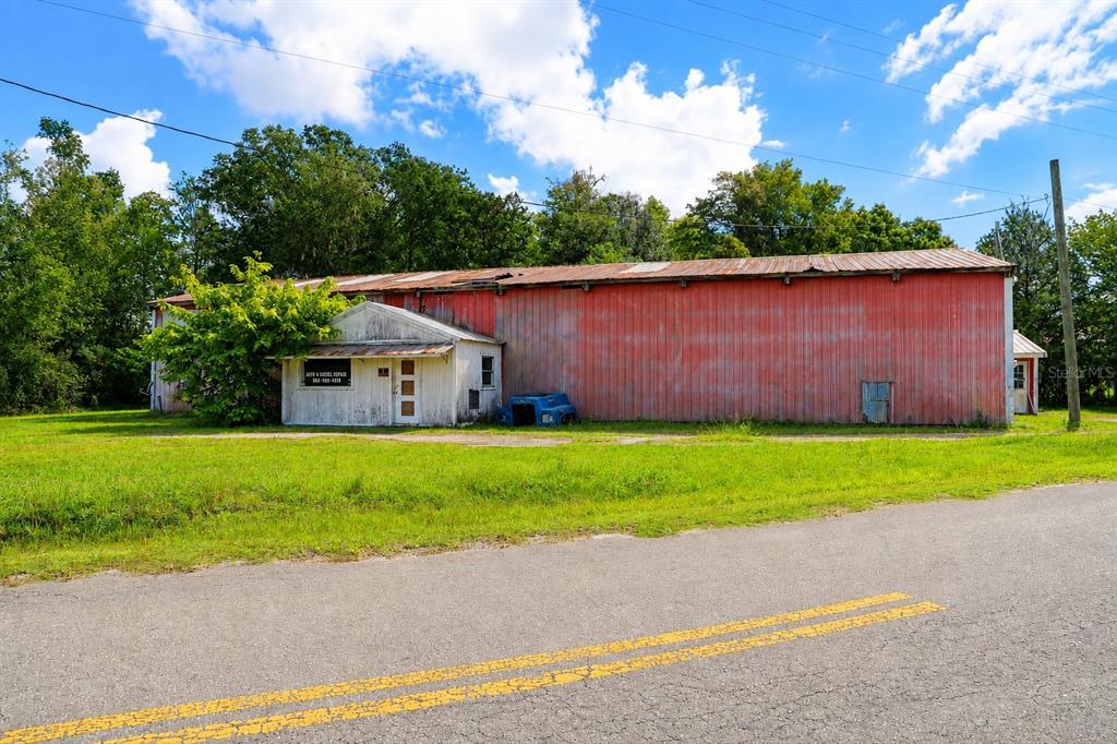 A long, red metal industrial building with a small white office entrance sits beside a road — 103 CONTAINER ROAD, STARKE, FL