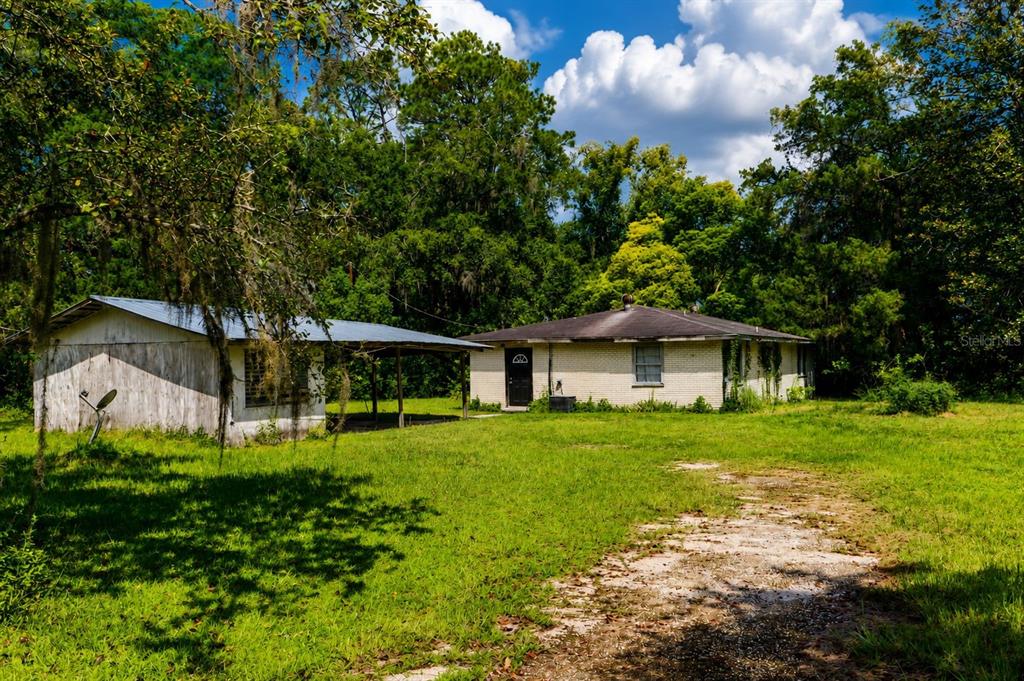 A single-story brick house with an attached carport sits on a grassy lot near trees — 103 CONTAINER ROAD, STARKE, FL