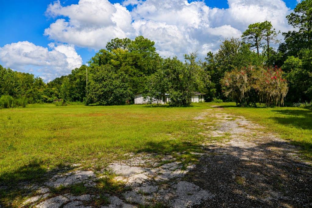 A gravel driveway leads toward a small, weathered house surrounded by trees and grassy fields — 103 CONTAINER ROAD, STARKE, FL