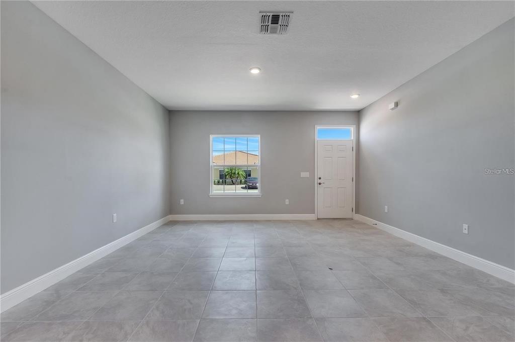 An empty room features gray walls, light-colored floor tiles, a window, and a white door — 1791 CORIANDER DRIVE UNIT 1791, POINCIANA, FL